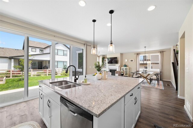 8261 Garden City Ave, Littleton, CO 80125 - kitchen featuring a sink, dishwasher, dark wood-style floors, an island with sink, and light stone counters