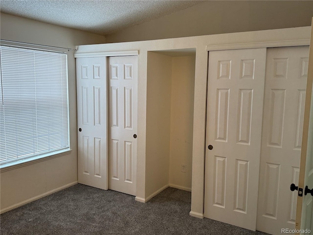 unfurnished bedroom featuring dark colored carpet, vaulted ceiling, two closets, and a textured ceiling