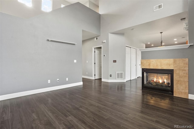 unfurnished living room featuring dark hardwood / wood-style floors, a high ceiling, and a tile fireplace