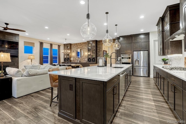2159 Bellcove Dr, Castle Pines, CO 80108 - kitchen featuring appliances with stainless steel finishes, wall chimney range hood, open floor plan, decorative backsplash, and dark brown cabinetry