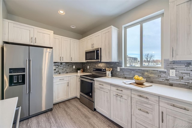 kitchen featuring appliances with stainless steel finishes, white cabinets, light wood-type flooring, and decorative backsplash