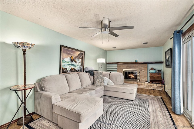 living room featuring ceiling fan, a brick fireplace, a textured ceiling, and light hardwood / wood-style flooring