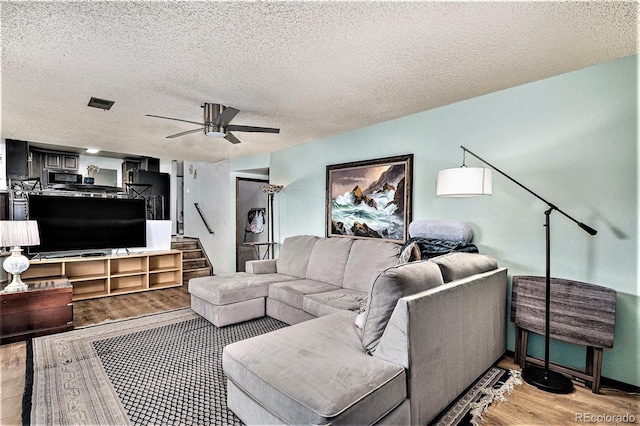 living room with ceiling fan, a textured ceiling, and light wood-type flooring