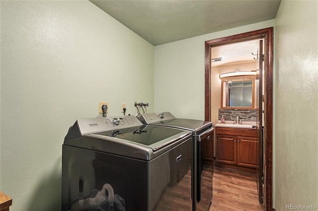 clothes washing area featuring sink, wood-type flooring, washing machine and dryer, and a textured ceiling