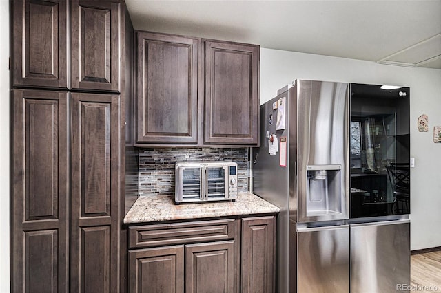 kitchen with dark brown cabinetry, light hardwood / wood-style flooring, stainless steel refrigerator, light stone countertops, and backsplash