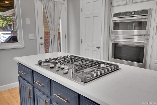 9880 E 157th Ave, Brighton, CO 80602 - kitchen with blue cabinets, appliances with stainless steel finishes, baseboards, and light wood finished floors
