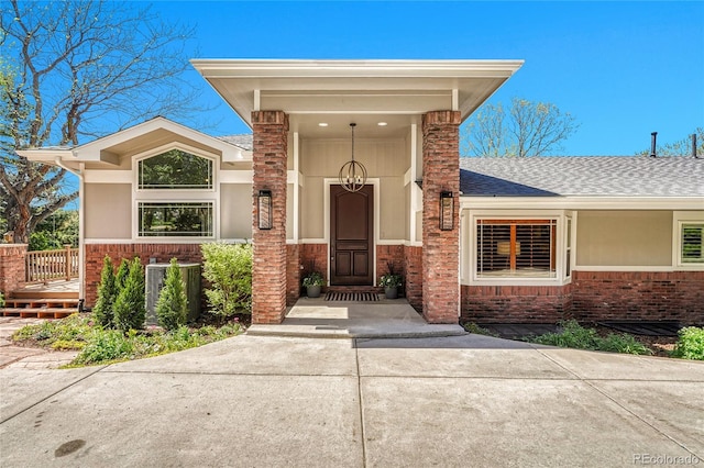 view of exterior entry with brick siding and roof with shingles