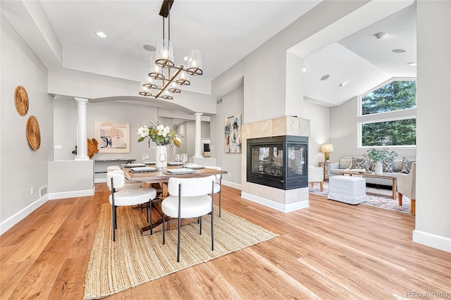 dining space featuring ornate columns, a multi sided fireplace, light wood finished floors, baseboards, and vaulted ceiling