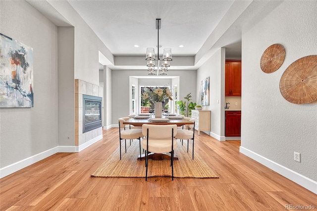 dining area with light wood-type flooring, a chandelier, a tile fireplace, a textured wall, and baseboards