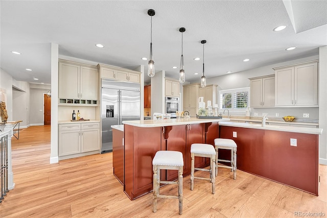 kitchen with appliances with stainless steel finishes, light wood-style floors, a spacious island, light countertops, and a breakfast bar area
