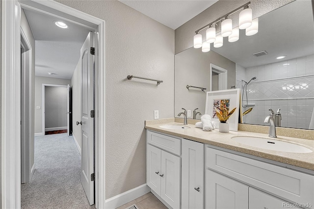 bathroom with a tile shower, double vanity, a textured wall, and baseboards