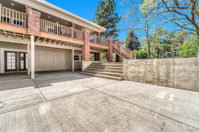 rear view of property with french doors, a carport, stairs, concrete driveway, and a patio