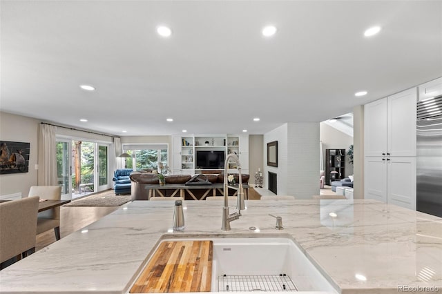 kitchen with white cabinetry, light stone countertops, sink, and a fireplace