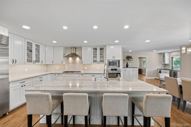 kitchen with a large island, wall chimney exhaust hood, appliances with stainless steel finishes, and white cabinets