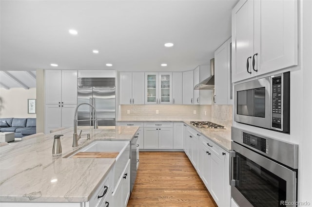 kitchen featuring built in appliances, sink, light stone countertops, white cabinets, and light hardwood / wood-style floors