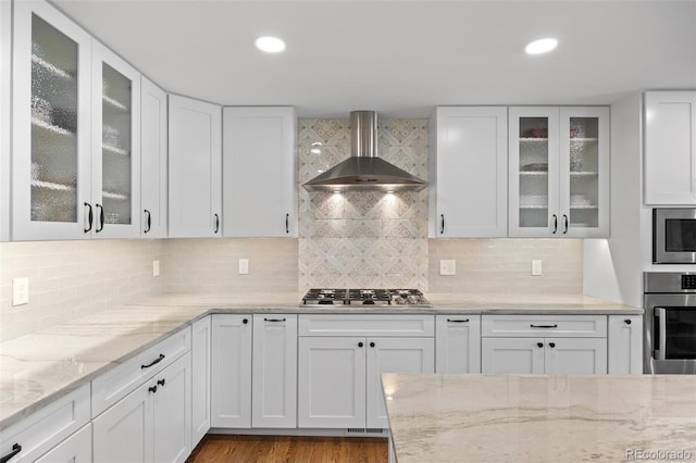 kitchen with wall chimney exhaust hood, appliances with stainless steel finishes, light stone counters, and white cabinets