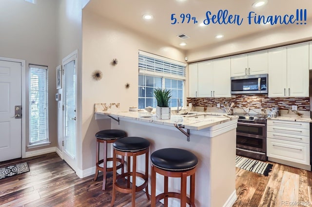 kitchen with appliances with stainless steel finishes, a breakfast bar, white cabinets, backsplash, and kitchen peninsula