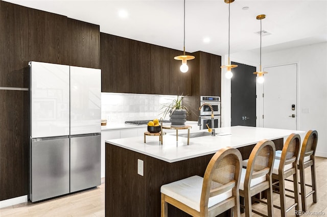 kitchen with light hardwood / wood-style flooring, decorative light fixtures, an island with sink, a breakfast bar, and appliances with stainless steel finishes