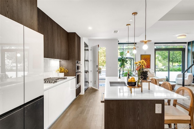 kitchen with light hardwood / wood-style flooring, stainless steel appliances, an island with sink, sink, and a breakfast bar