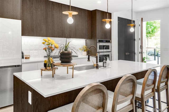 kitchen with decorative light fixtures, a kitchen breakfast bar, sink, appliances with stainless steel finishes, and a center island with sink