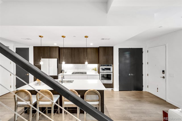 kitchen with light wood-type flooring, backsplash, stainless steel appliances, and dark brown cabinetry