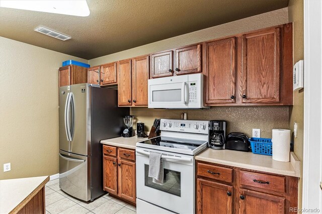 kitchen with white appliances, light tile patterned floors, and a textured ceiling