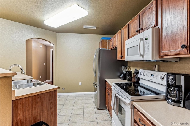 kitchen with sink, white appliances, light tile patterned floors, and a textured ceiling