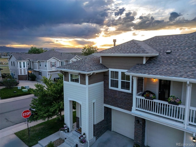 12910 Grant Cir W Unit C, Thornton, CO 80241 - view of front of house featuring stone siding, roof with shingles, a garage, concrete driveway, and a balcony
