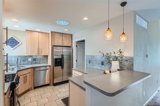 kitchen with appliances with stainless steel finishes, kitchen peninsula, light brown cabinets, pendant lighting, and sink