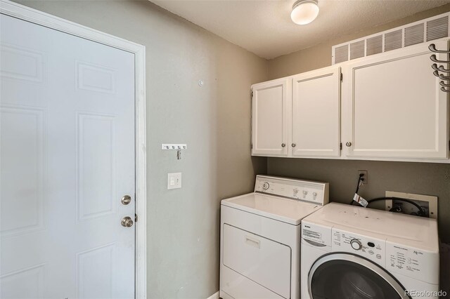 washroom with cabinets, a textured ceiling, and washing machine and dryer