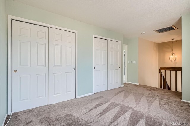 unfurnished bedroom with an inviting chandelier, two closets, a textured ceiling, and carpet flooring