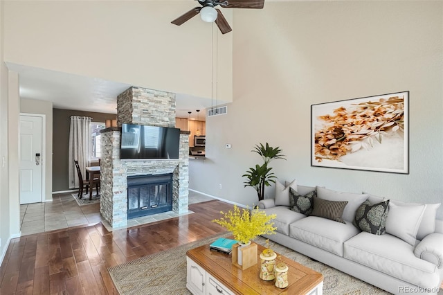 living room featuring wood-type flooring, a stone fireplace, and ceiling fan