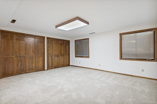 unfurnished bedroom featuring light carpet and two closets