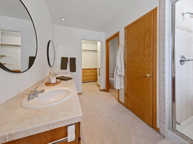 bathroom with double vanity, a stall shower, a sink, a spacious closet, and toilet