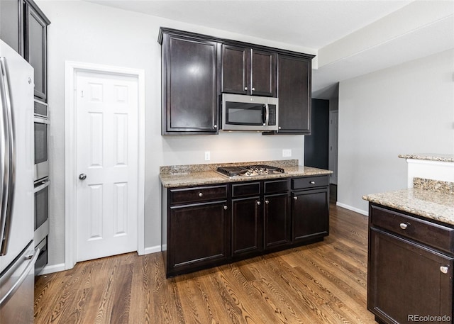 kitchen featuring appliances with stainless steel finishes, dark brown cabinets, dark hardwood / wood-style floors, and light stone countertops