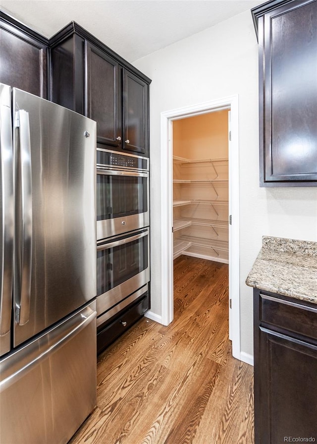 kitchen featuring light hardwood / wood-style flooring, stainless steel appliances, light stone countertops, and dark brown cabinetry