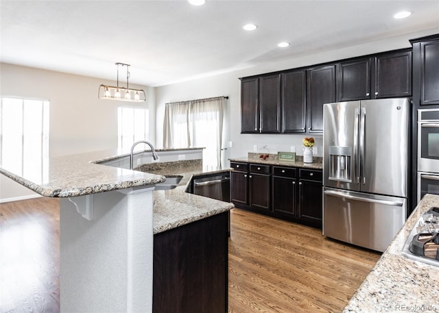 kitchen featuring pendant lighting, wood-type flooring, sink, appliances with stainless steel finishes, and light stone countertops