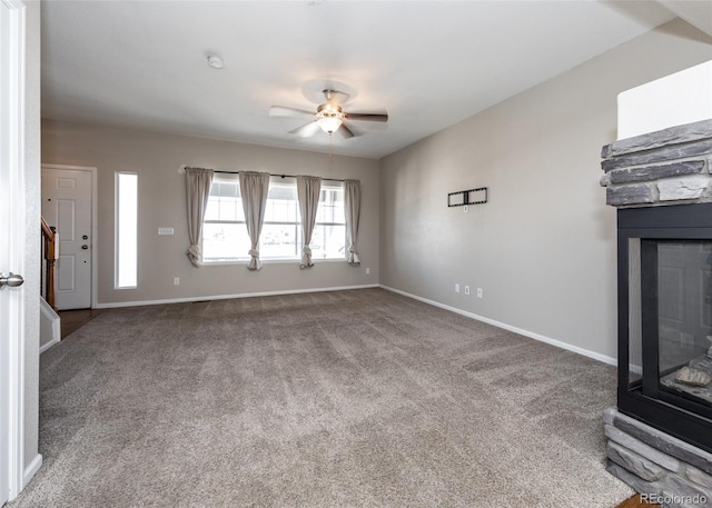 unfurnished living room featuring ceiling fan, a stone fireplace, and carpet flooring