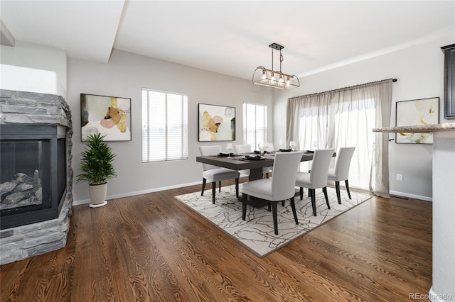 dining area with a notable chandelier, dark hardwood / wood-style floors, and a stone fireplace