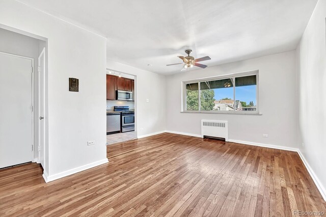 unfurnished living room featuring light hardwood / wood-style floors, ceiling fan, and radiator heating unit