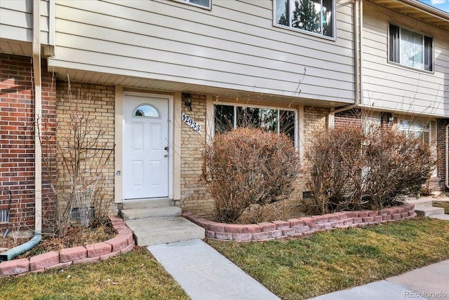 entrance to property with brick siding and a lawn