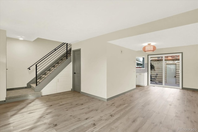 spare room with light wood-style floors, baseboards, and stairway