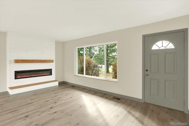 foyer featuring light wood-type flooring, a glass covered fireplace, visible vents, and baseboards