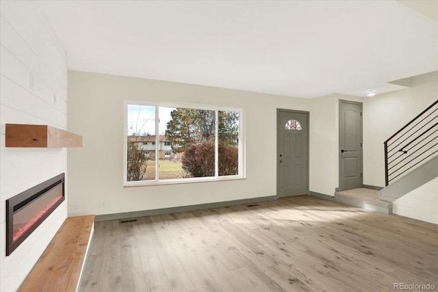 unfurnished living room with a fireplace, visible vents, baseboards, stairs, and light wood finished floors