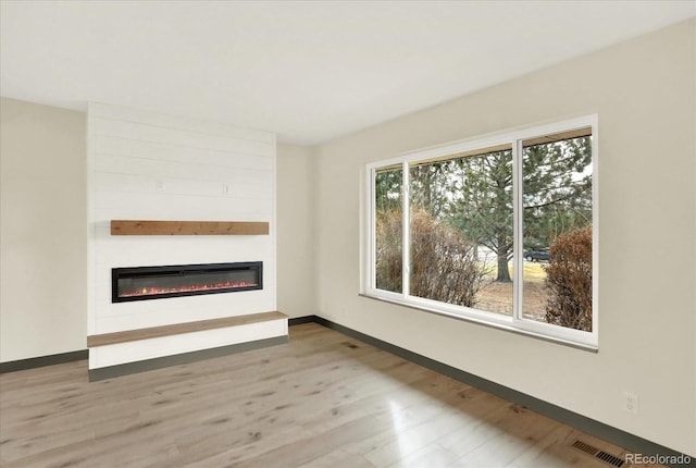 unfurnished living room with a fireplace, wood finished floors, visible vents, and baseboards