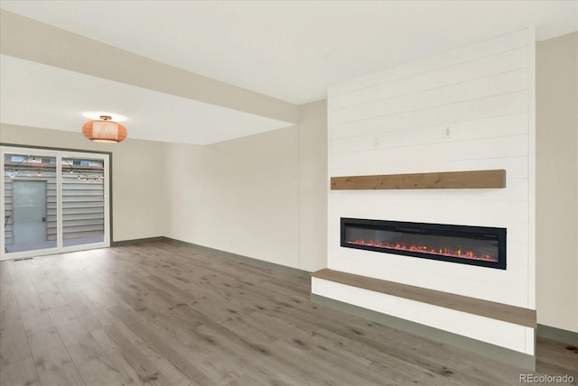 unfurnished living room featuring a glass covered fireplace, dark wood finished floors, and baseboards