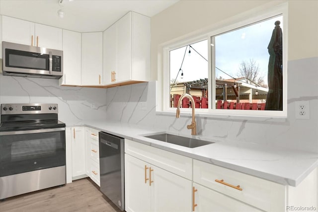 kitchen featuring light stone counters, a sink, white cabinetry, appliances with stainless steel finishes, and light wood-type flooring