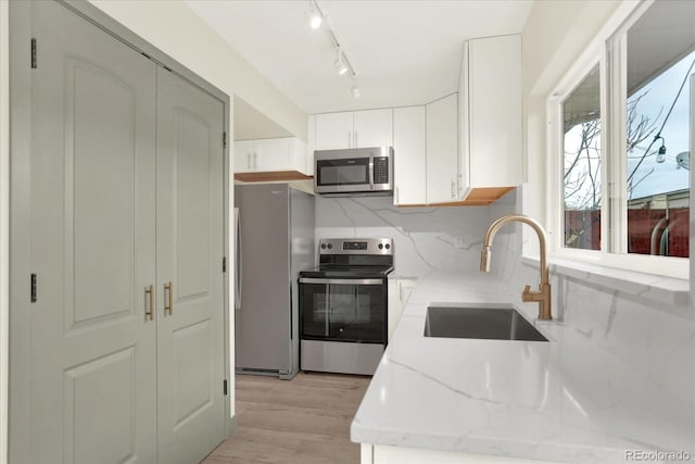 kitchen featuring a sink, white cabinets, appliances with stainless steel finishes, light stone countertops, and light wood finished floors