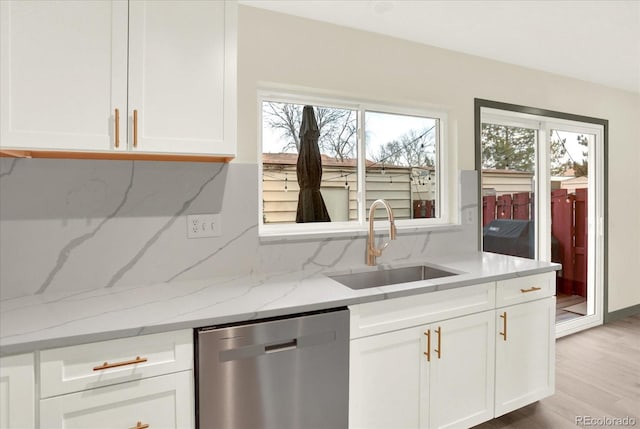 kitchen featuring light stone counters, white cabinets, dishwasher, and a sink