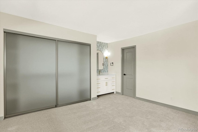 unfurnished bedroom featuring ensuite bath, baseboards, a closet, and light colored carpet